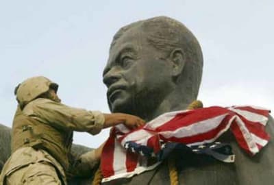 Amerikansk soldat virar en amerikansk flagga runt staty av Saddam Hussein