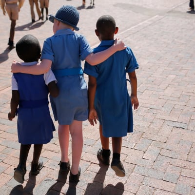 Kolme lasta kävelee kaulakkain lesotholaisessa koulussa.