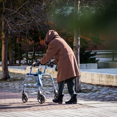 En äldre person går med rollator.