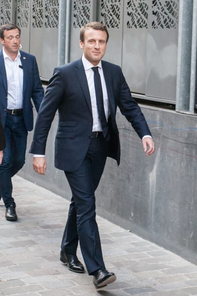 Emmanuel Macron som går på gatan, tittar in i kameran och ler.