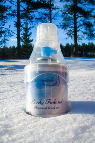 En flaska med frisk luft från Finland nedstucken i snön med träd i bakgrunden