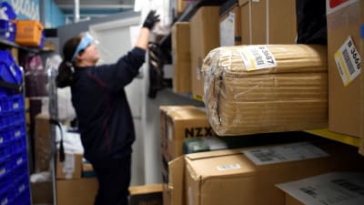 En person plockar upp paket i hyllan i en mataffär.