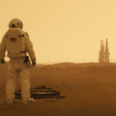 En astronaut på avstånd blickar ut över det karga Marslandskapet.