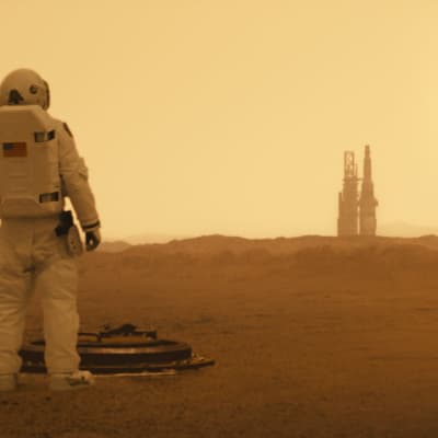 En astronaut på avstånd blickar ut över det karga Marslandskapet.