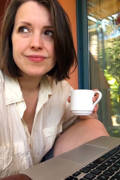 Författaren Eva Frantz sitter vid sin bärbara dator och håller i en kaffemugg i handen. 