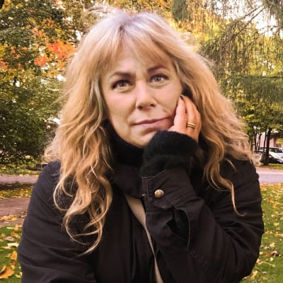 Stina Wollter lutar mot en gravsten i en höstig park i Helsingfors.