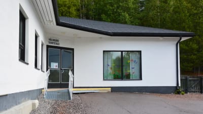 En vit byggnad med svarta detaljer. Ovanför ingången står det hälsogård terveystalo.