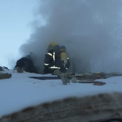 Rökdykare i Fiskars sitter på ett snöigt tak, där massor av gråsvart rök bolmar ut.