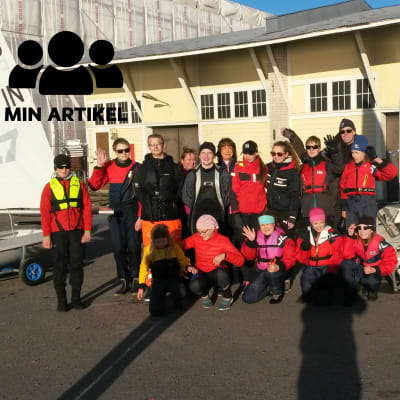 Ett gruppfoto av ett gäng med seglingsjuniorer. I bakgrunden syns en gul byggnad.