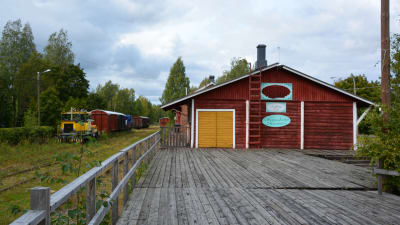 Till vänster tågspår och tågvagnar, till höger en röd träbyggnad med skylten Magasinboden.