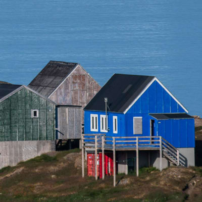 En bild på Grönland med ett litet isberg och hus.