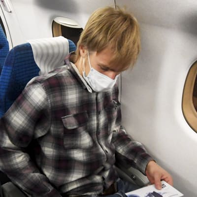 En person på ett Finnairplan i ett flygsäte. Killen är iklädd i munskydd.