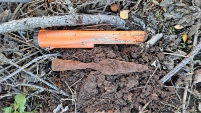 En spjutspets ligger på en bädd av nyuppgrävd jord intill ett modernt verktyg.