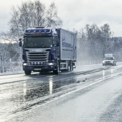 Lastbilar och personbilar på en våt landsväg på vintern.