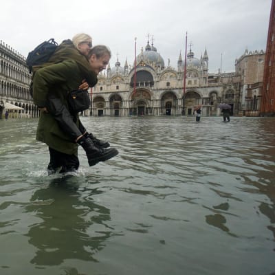 En man bär en kvinna över en översvämmad Piazza San Marco i Venedig.