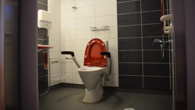 Nya Almahemmets rymliga toalett med dusch och gråa och vita kakel på väggarna.