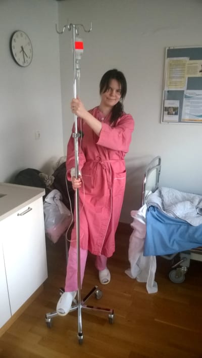 Pernilla Bergman står med en droppställning i sitt sjukhusrum