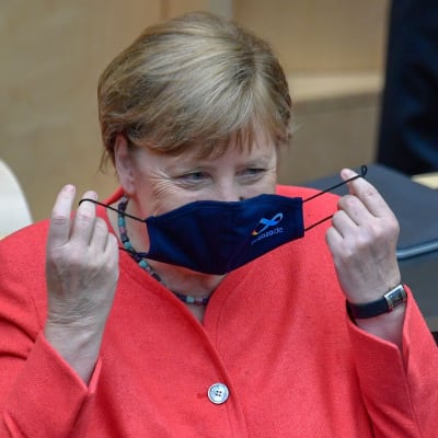 Angela Merkel sätter på sig ett munskydd med tysk EU-logo. 