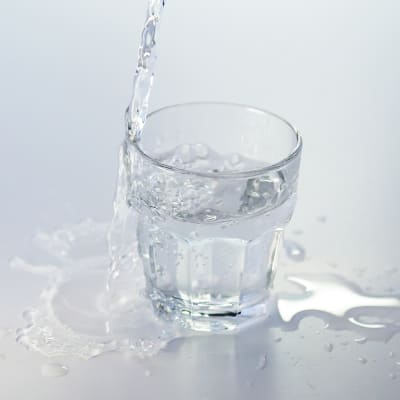 Vatten som rinner ner i ett glas. En del av vattnet rinner över och bildar pölar.