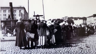 En svartvit bild av en lång brödkö på Salutorget i Helsingfors på 1910-talet.