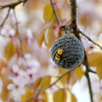 En virkad boll som ser ut som ett getingbo är upphängt i ett träd som blommar.