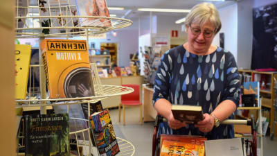 Bibliotekschef Eija Sjöblom ser ner i en bok intill en bokställning.