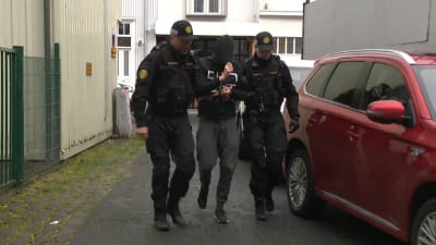 Två poliser bär på en man som har en luva på huvudet.