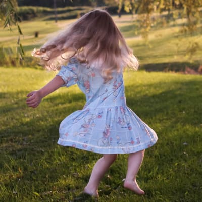 Flicka som springer på gräsmatta i sommarljus.