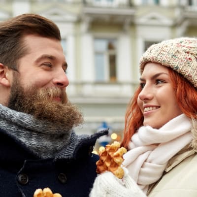 En man med skägg och en kvinna tittar på varandra. Båda ler och har varsin våffla i handen.