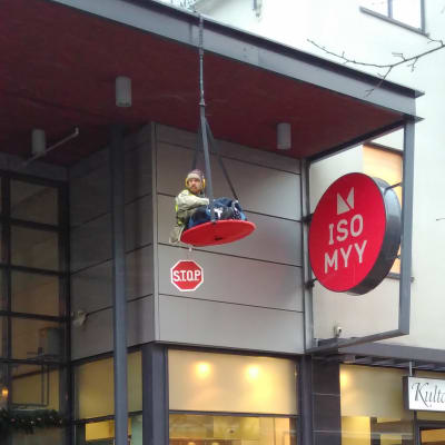 Mielenosoittaja roikkuu kauppakeskuksen sisäänkäynnin yläpuolella Joensuussa.