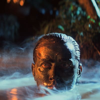 Benjamin Willards (Martin Sheen) huvud dyker upp ur vattenytan, ansiktet är svartmålat och det vattnet ryker av ånga.