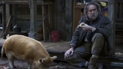 Rob (Nicolas Cage) sitter på en trappa utomhus och äter en pajbit medan en gris vid hans fötter äter ur en stekpanna.
