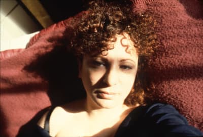 Närbild på en trött Nan Goldin som ligger i sängen och fotografera sig själv rakt uppifrån.