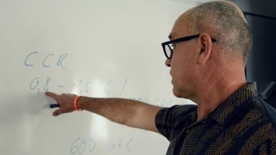 John Hassler pekar mot några siffror och bokstäver han antecknat på en whiteboard.