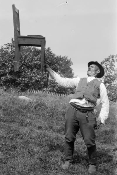 En man lyfter en stol med sin ena hand. Bilden är tagen 1929 i Kungsböle, Strömfors.