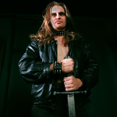 Lasse Grönroos poserar i läderrock, bart bröst och med ett svärd i handen.
