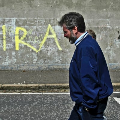IRA:n aiempana poliittisena siipenä pidetyn Sinn Fein -puolueen johtaja Gerry Adams kävelee jatkuvuus-IRA:ngraffitin ohi Belfastissa vuonna 2005.