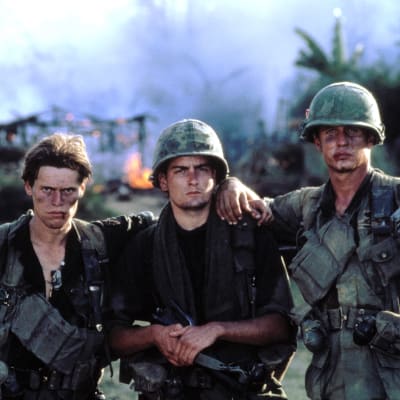 Kolme nuorta jalkaväensotilasta sotatantereella, likaisissa univormuissaan aseet olalla, pitävät käsiään toistensa hartioilla.