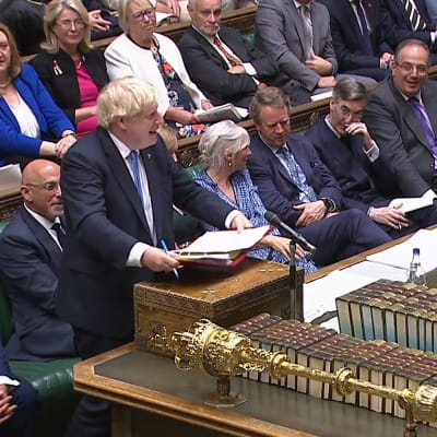Boris Johnson talar i brittiska underhuset. Omkring honom sitter andra parlamentsledamöter och på bordet framför ligger en spira och böcker.