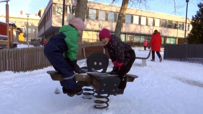 Två flickor gungar på en gunga på en dagisgård. 