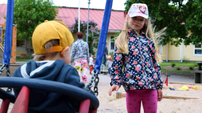 En flicka gungar ett mindre barn som har gul keps på sig på Hulta dagisgård.