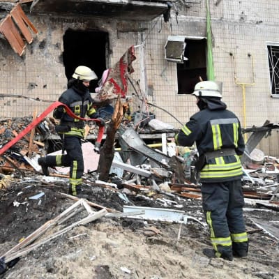 Brandmän röjer bort skrot vid en förstörd höghusbyggnad i Kiev.