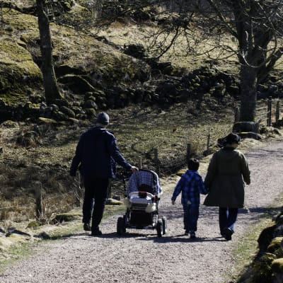 Två vuxna och två barn, ett i barnvagn, ute på promenad i naturen.