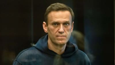 Aleksei Navalnyj i mörkblå munktröja i sin cell där han står och bevakas av en vakt.