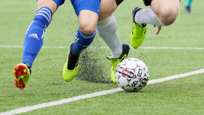 Gummigranulat flyger i luften under fotbollsmatch.
