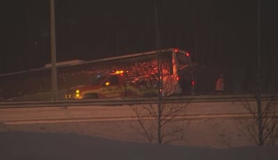 På andra sidan en motorväg har en buss kört i diket i mörker och snö. Intill bussens bakända står en bärgningsbil.