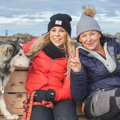 Krista och Lotta och en hund sitter på en bänk ute i Lappland.