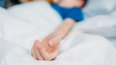 En liten pojke ligger i en sjukhussäng med sin ena arm utsträckt.