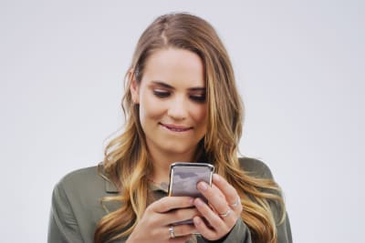Småleende ung kvinna ser på sin telefon