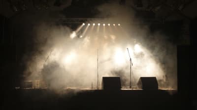 Tre mikrofoner syns på en scen bakom en rökridå